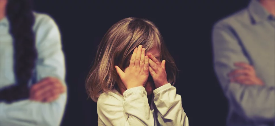 A child covering her face with hands as parents think about custody